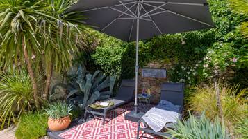 A patio with a red patterned rug, two lounge chairs, a table, and a large umbrella.