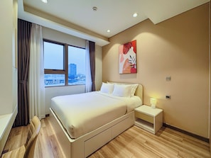 Una habitación de hotel moderna con una cama grande, una mesita de noche, una ventana con cortinas, vistas a la ciudad y una obra de arte colgada en la pared.