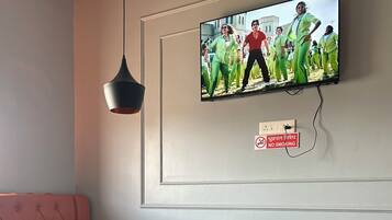 A restaurant interior with a television mounted on the wall displaying a group of people dancing, a 'No Smoking' sign, a cushioned booth, and a wooden table with chairs.