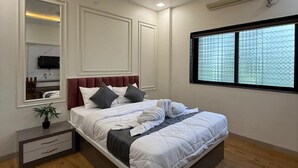 A modern bedroom with a bed, bedside tables, a ceiling fan, an air conditioning unit, and a window with a view. - Hotel Chaufula Garden Lodging (Shirur)