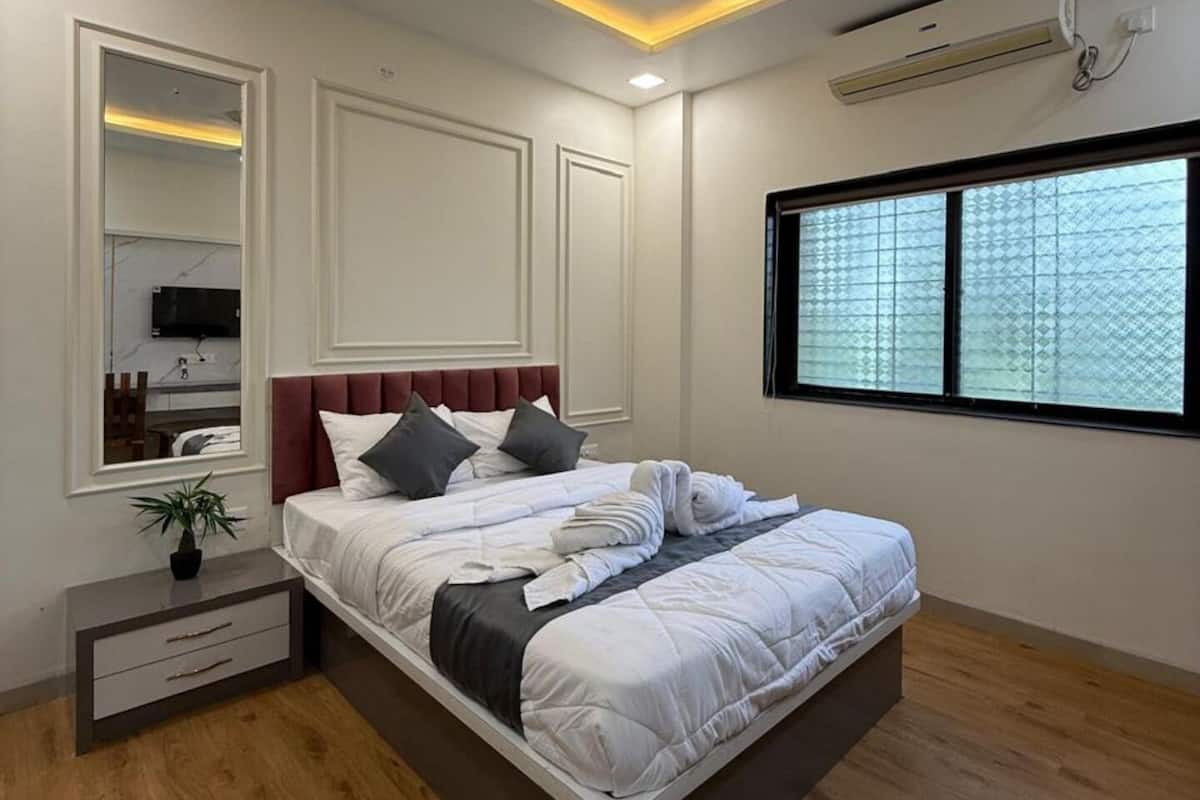 A modern bedroom with a bed, bedside tables, a ceiling fan, an air conditioning unit, and a window with a view.