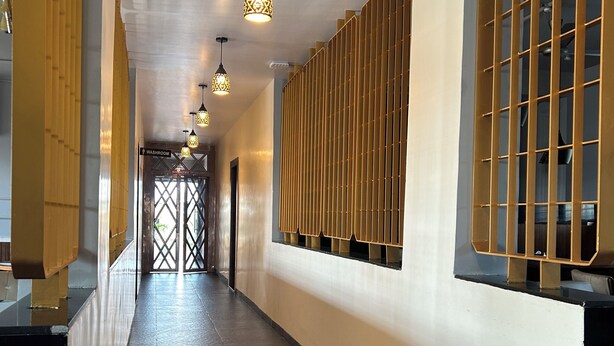 A hallway with a tiled floor, a washroom sign, and a decorative wall with vertical panels. - Hotel Chaufula Garden Lodging (Shirur)