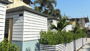 A residential area with white wooden houses, a paved walkway, and lush greenery. - Hotel Chaufula Garden Lodging (Shirur)