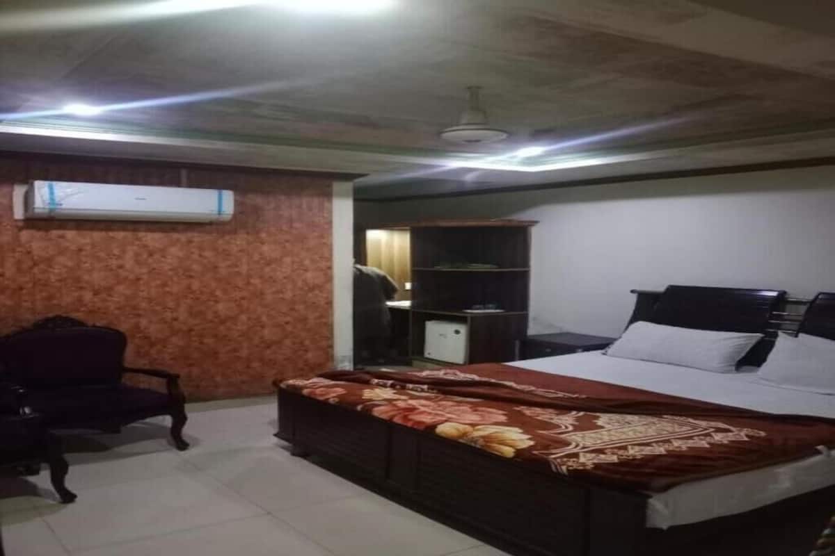A bedroom with a bed, a chair, a wardrobe, and an air conditioning unit.