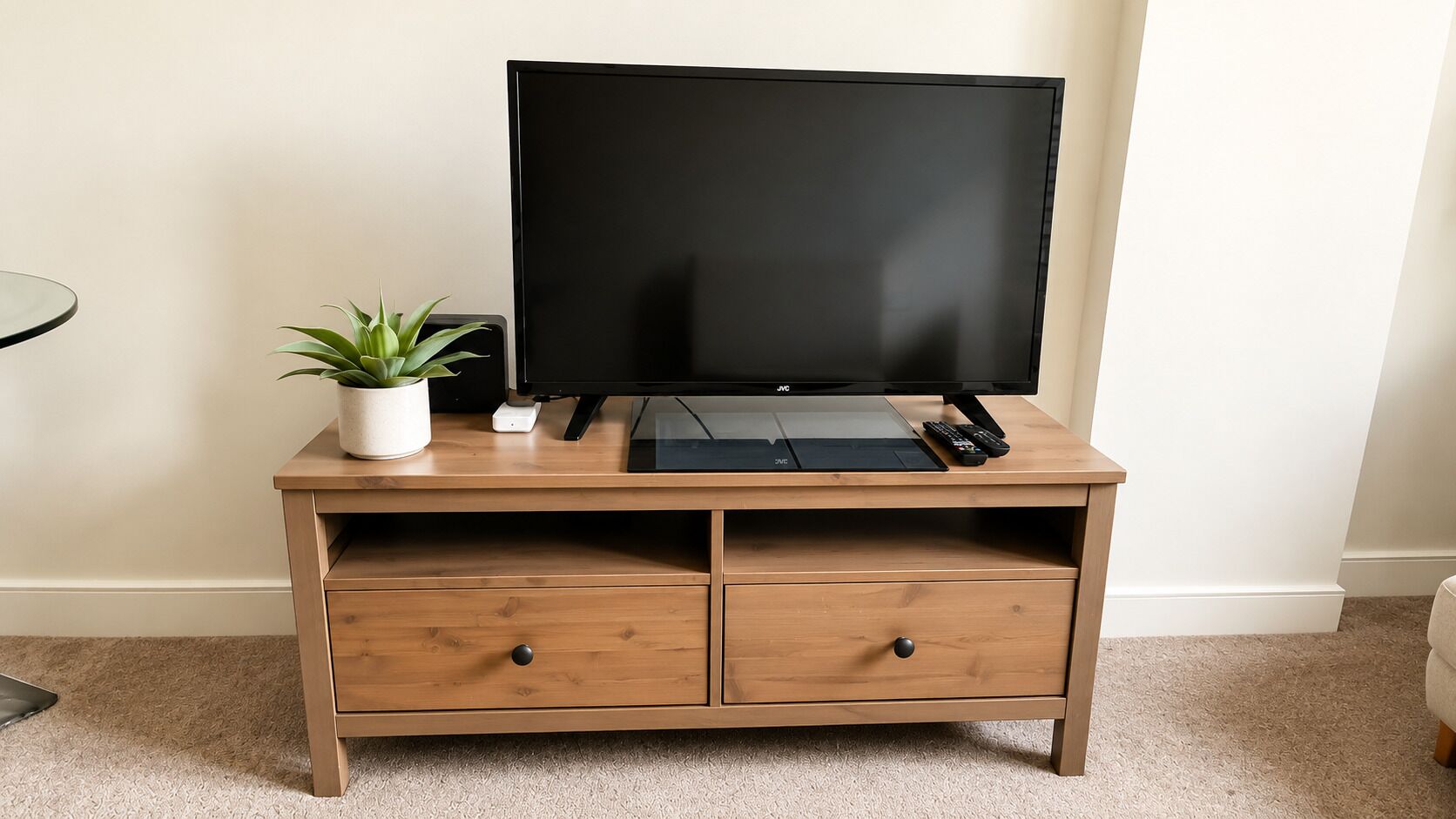 Un mobile TV in legno con televisore piatto, due cassetti, una piccola pianta in vaso e un telecomando.