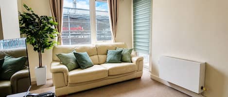 A living room with a beige sofa, a potted plant, and a radiator.