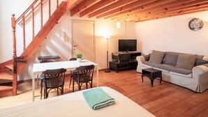 Eine Holztreppe, ein Essbereich mit Stühlen, ein Sofa, ein Fernseher und eine Lampe.