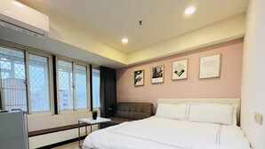 A hotel room with a bed, a desk, a chair, a window with a view, and framed pictures on the wall. - STAG Haven (Taipei)