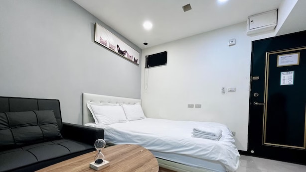 A modern hotel room with a bed, a sofa, a small table, and a wall-mounted picture. - STAG Haven (Taipei)