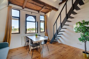 A room with a wooden floor, a table with chairs, a potted plant, and a staircase. - Two-bedroom apartment by the river (Antwerp)