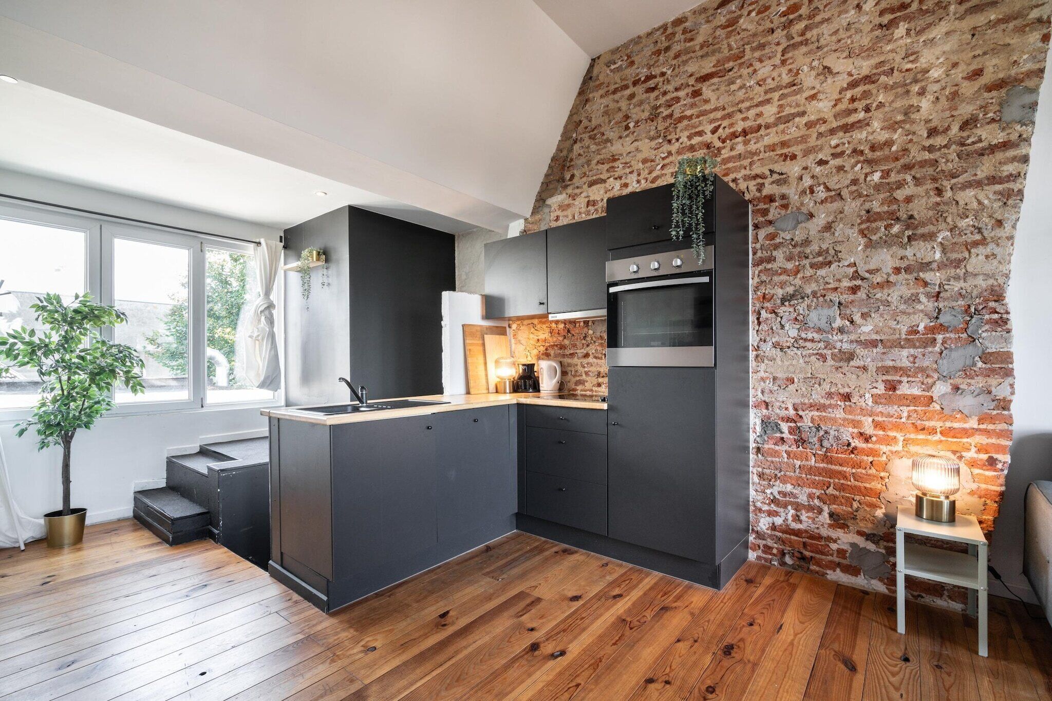 Een moderne keuken met een bakstenen muur, houten vloer en een inbouw kookeiland.
