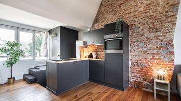 Een moderne keuken met een bakstenen muur, houten vloer en een inbouw kookeiland.