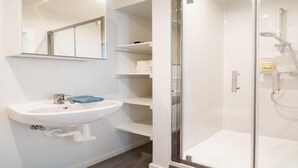 Un baño moderno con lavamanos blanco, espejo y ducha con mampara de vidrio.