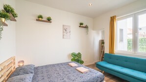 Un dormitorio con cama, sofá azul y estanterías con plantas.