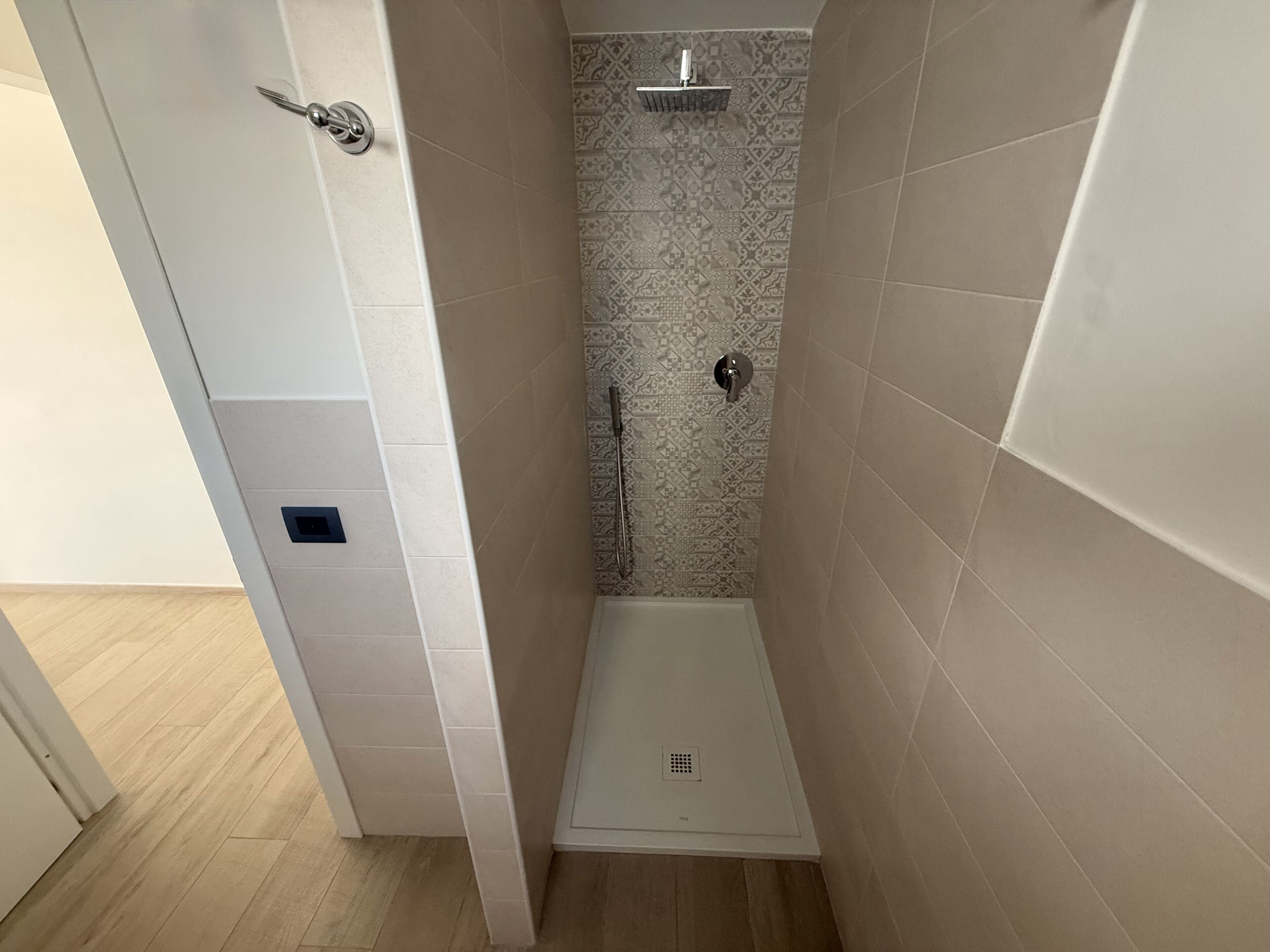 A small, enclosed shower area with patterned tiles, a showerhead, and a control panel.