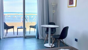 Habitación de hotel con cama, una mesa, dos sillas, vista al mar y un cuadro en la pared.