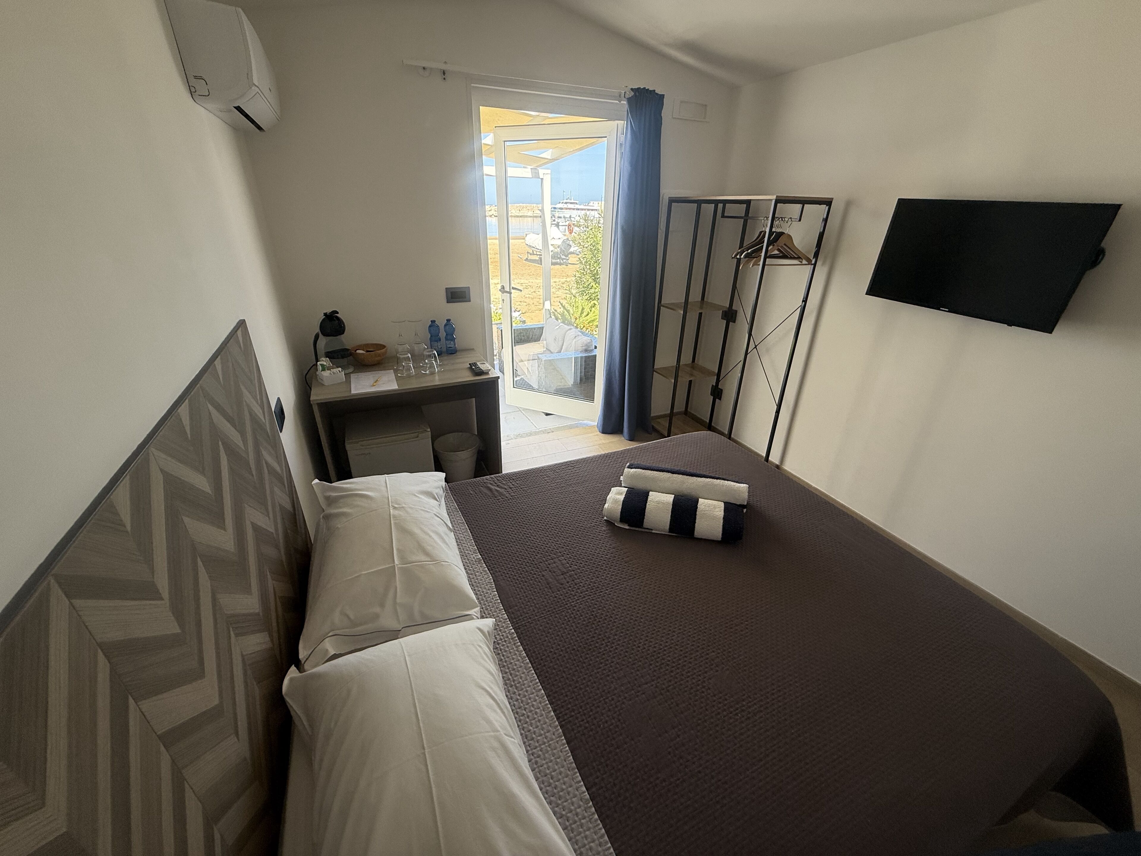 A hotel room with a bed, a desk, a chair, a TV, and a balcony with a view.