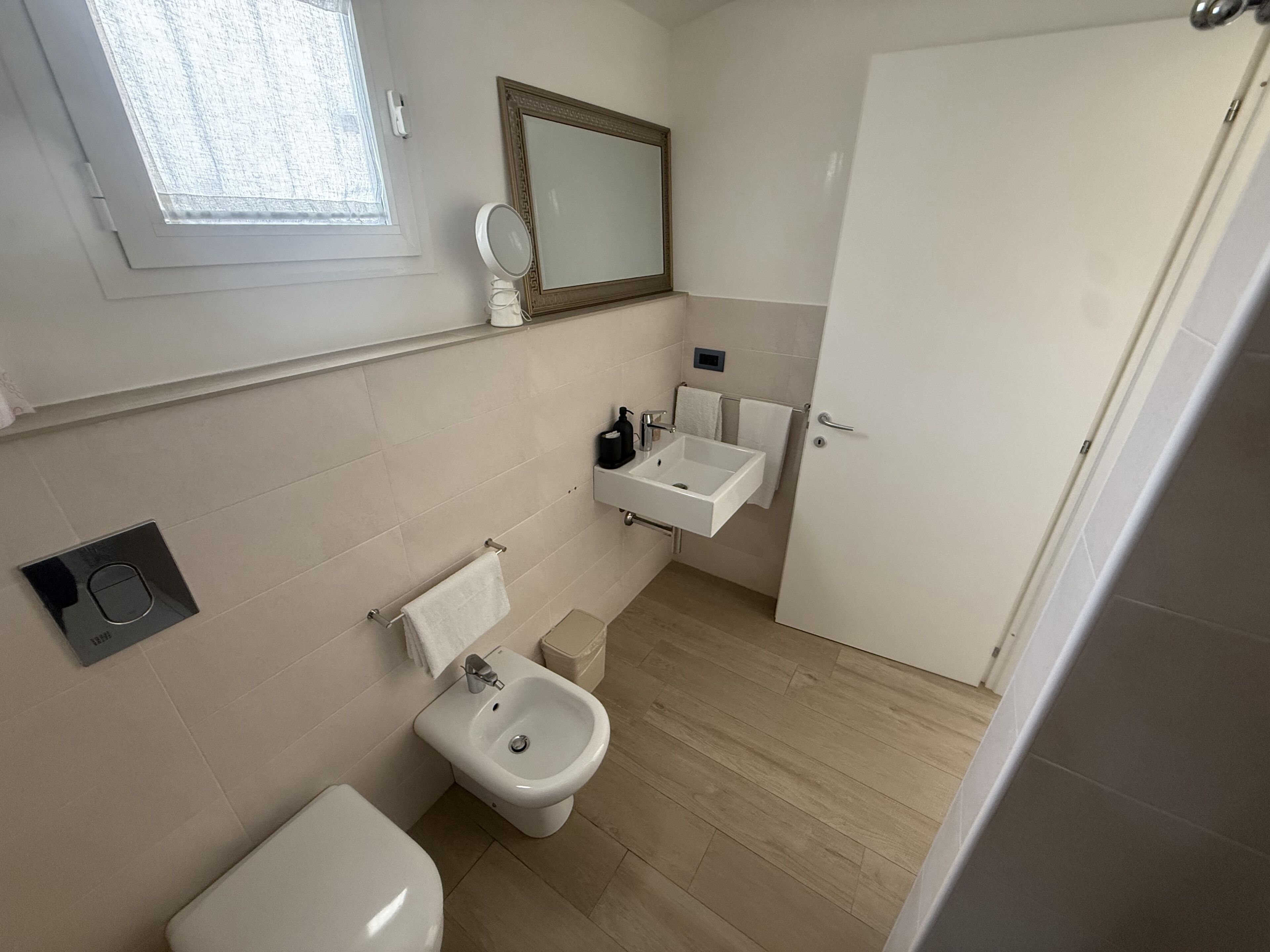 A bathroom with a toilet, bidet, sink, mirror, and a door.