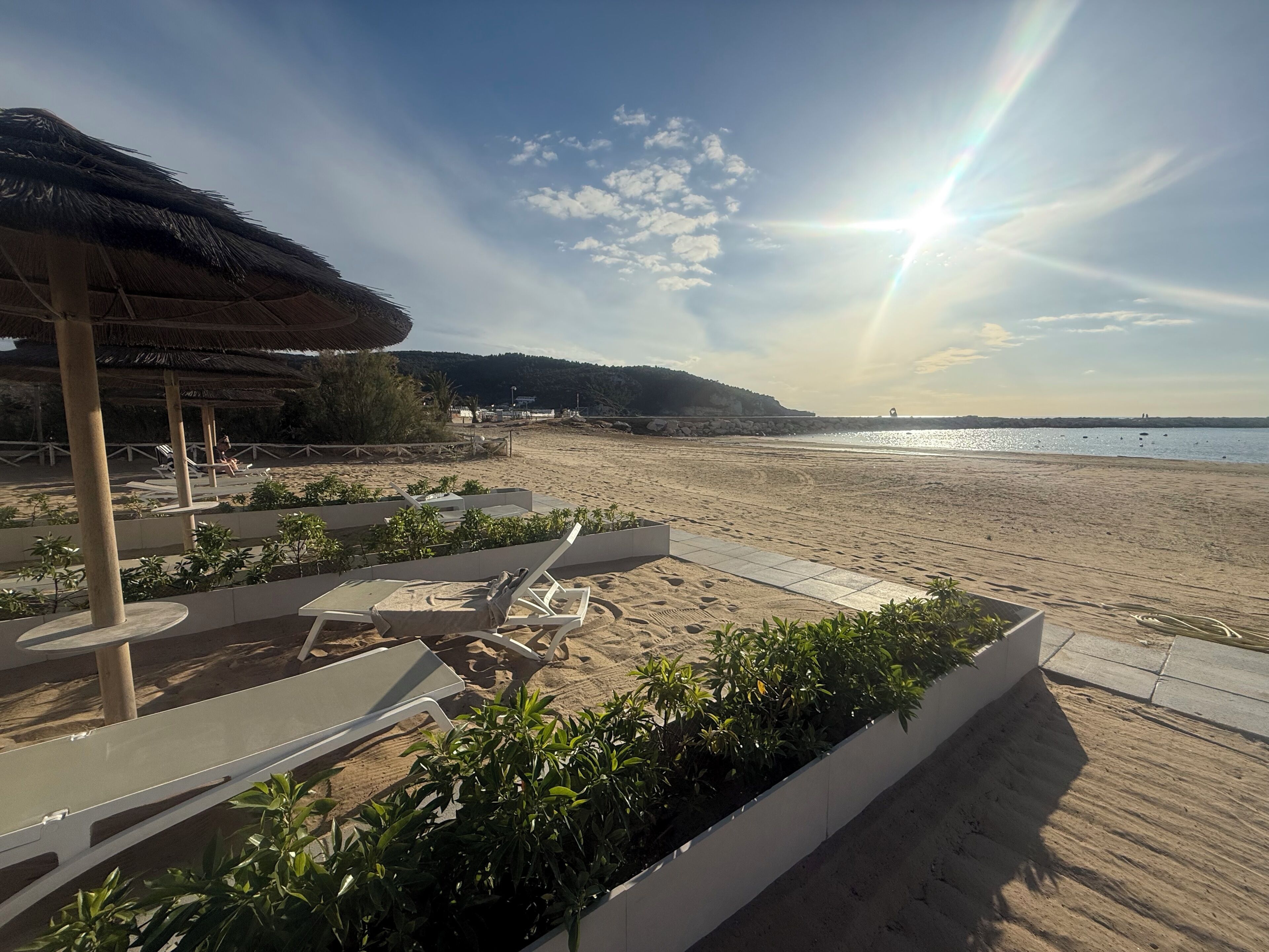A beach resort with lounge chairs, a thatched-roof structure, and a view of the sea.