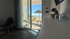 Una habitación con puerta de cristal corrediza que da a un balcón con vista a la playa y una sombrilla de paja.