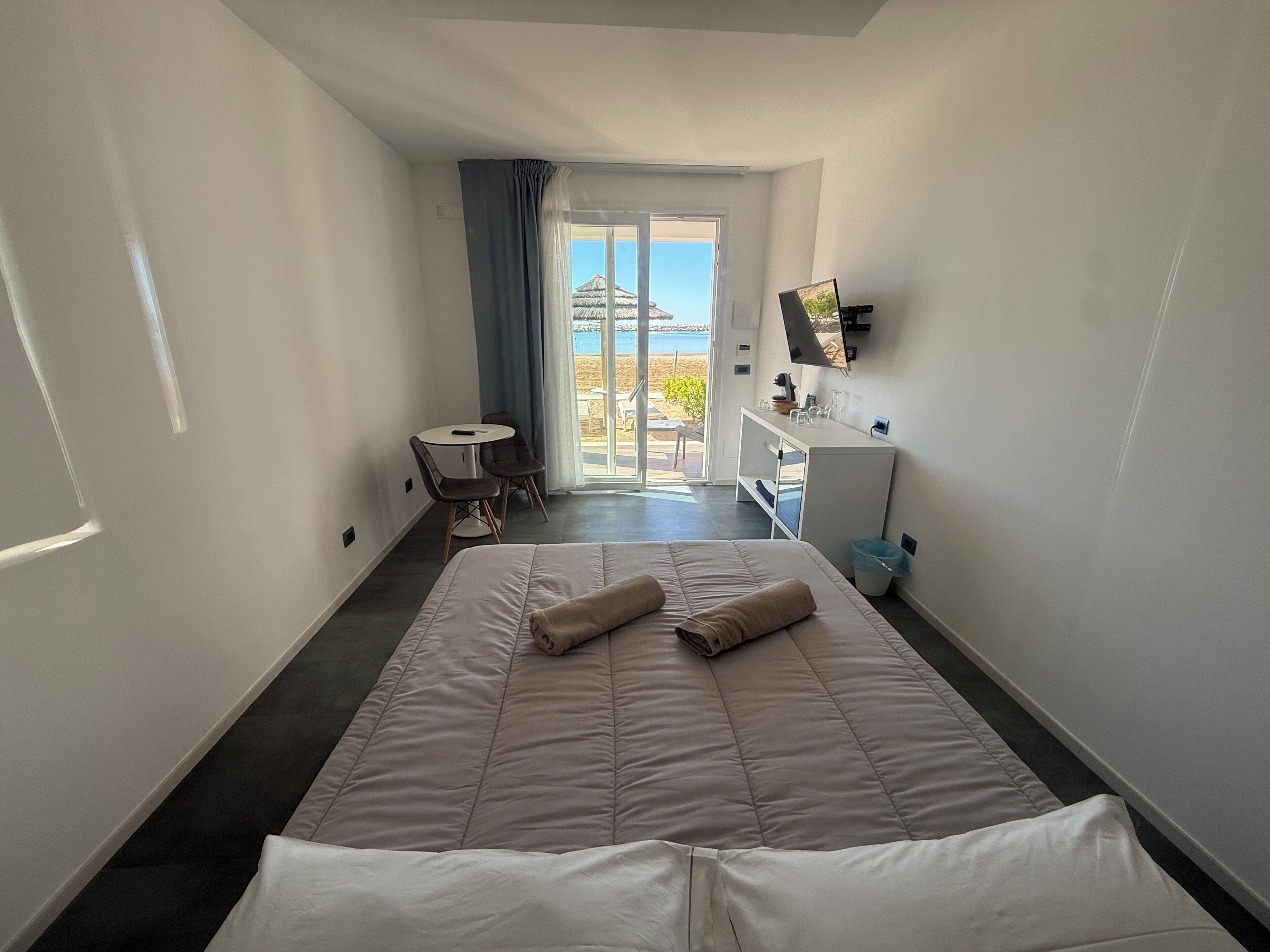 Une chambre d’hôtel avec un lit, un bureau, une chaise, une télévision et une vue sur la plage.