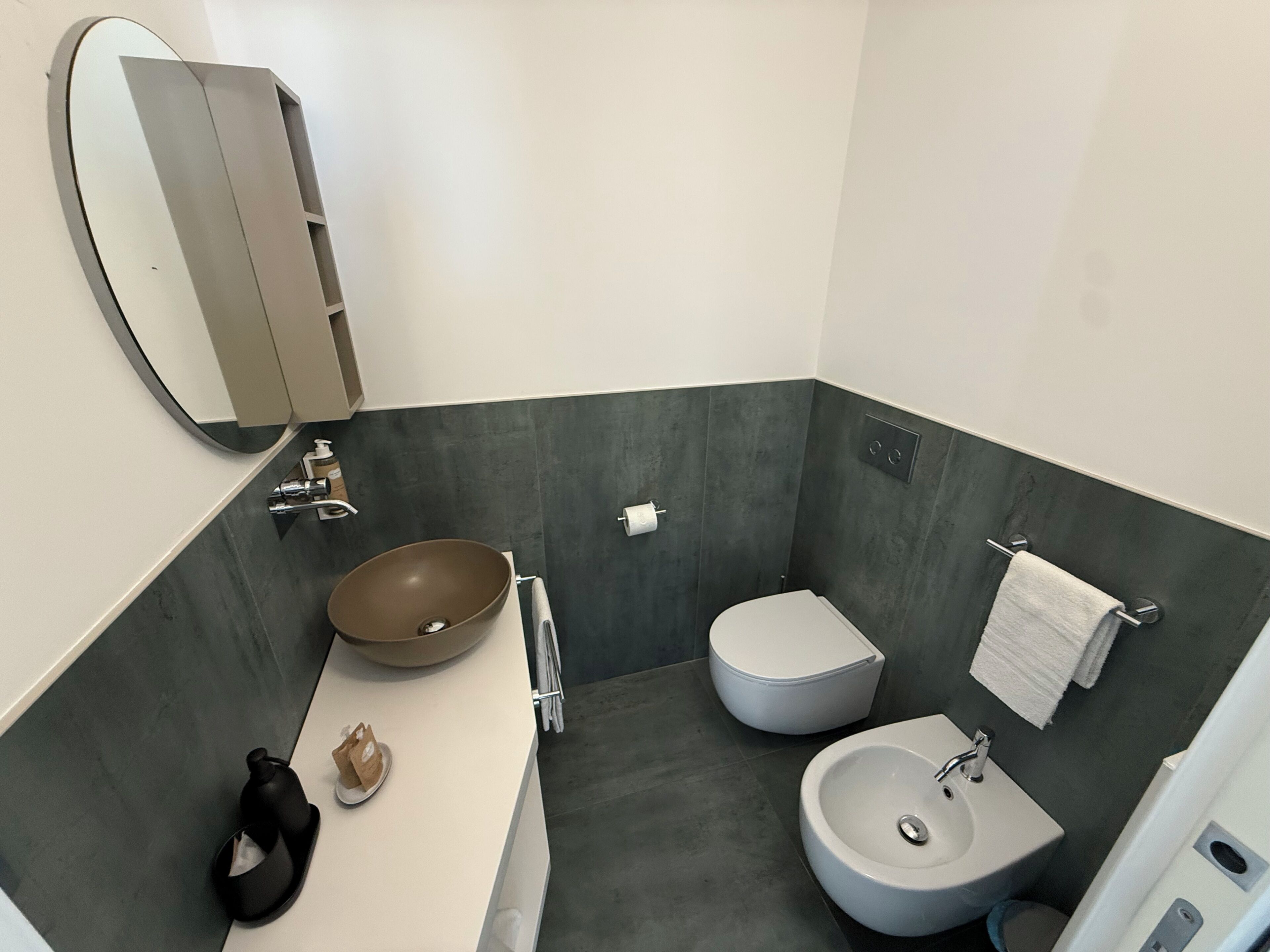 Une salle de bain moderne avec un grand miroir, un lavabo sur colonne, des toilettes et un autre lavabo posé sur un socle.