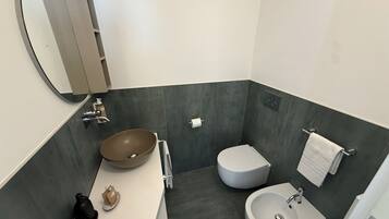 Une salle de bain moderne avec un grand miroir, un lavabo sur colonne, des toilettes et un autre lavabo posé sur un socle.