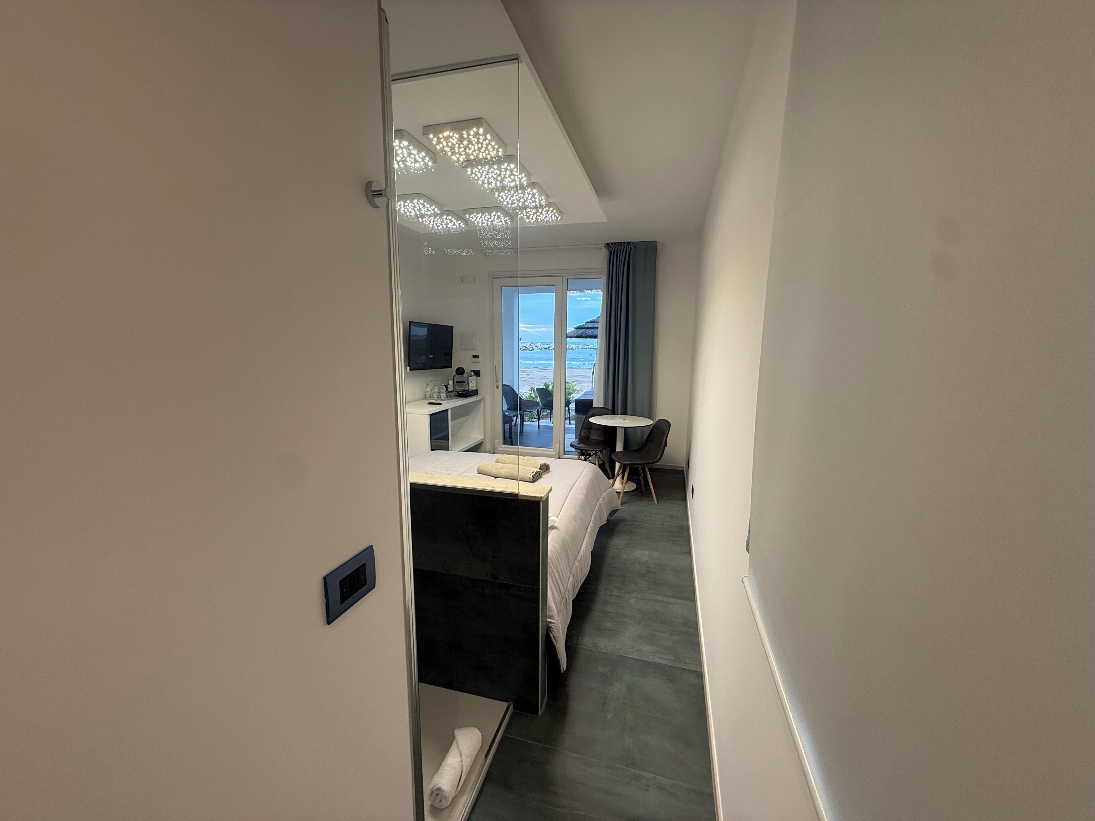 Une chambre d’hôtel avec un lit, un bureau équipé d’un ordinateur, une télévision et une vue sur la mer.