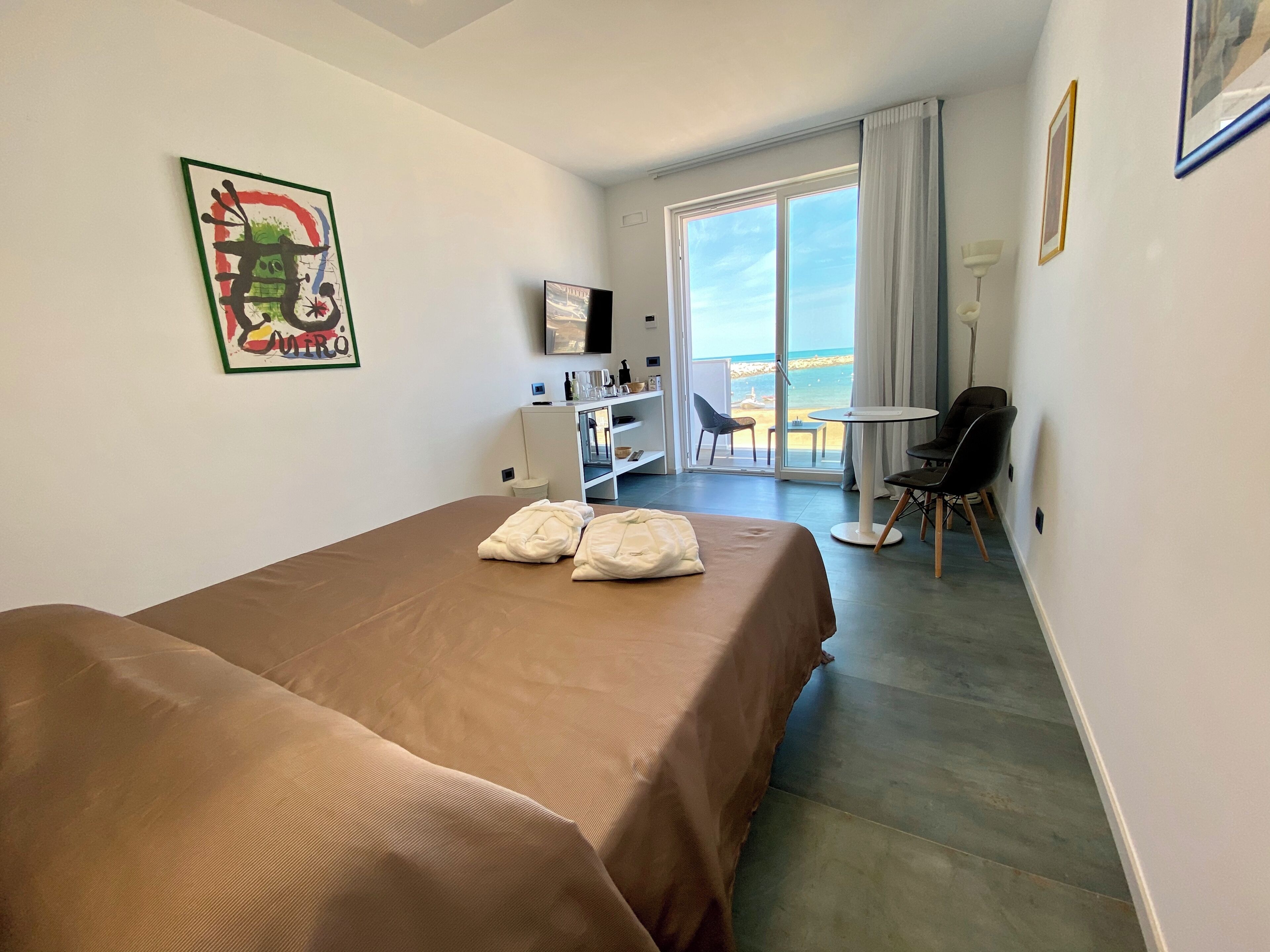 Een hotelkamer met twee bedden, een bureau, een stoel, een televisie en een balkon met uitzicht op het strand.