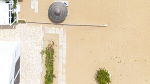 Vista aérea de un hotel frente a la playa, con mesas al aire libre, sombrillas y un camino empedrado.