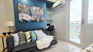 A modern living room with a black sofa, colorful cushions, a large abstract painting, a laptop on a side table, and a view of a balcony. - Cozy 2-bedroom condo w/AC living room, balcony, Netflix walking dis to SM North (Quezon City)