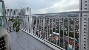 A balcony with a metal railing, a potted plant, and a view of a cityscape with buildings. - Cozy 2-bedroom condo w/AC living room, balcony, Netflix walking dis to SM North (Quezon City)