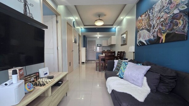 A living room with a TV, chess set, and a sofa. - Cozy 2-bedroom condo w/AC living room, balcony, Netflix walking dis to SM North (Quezon City)