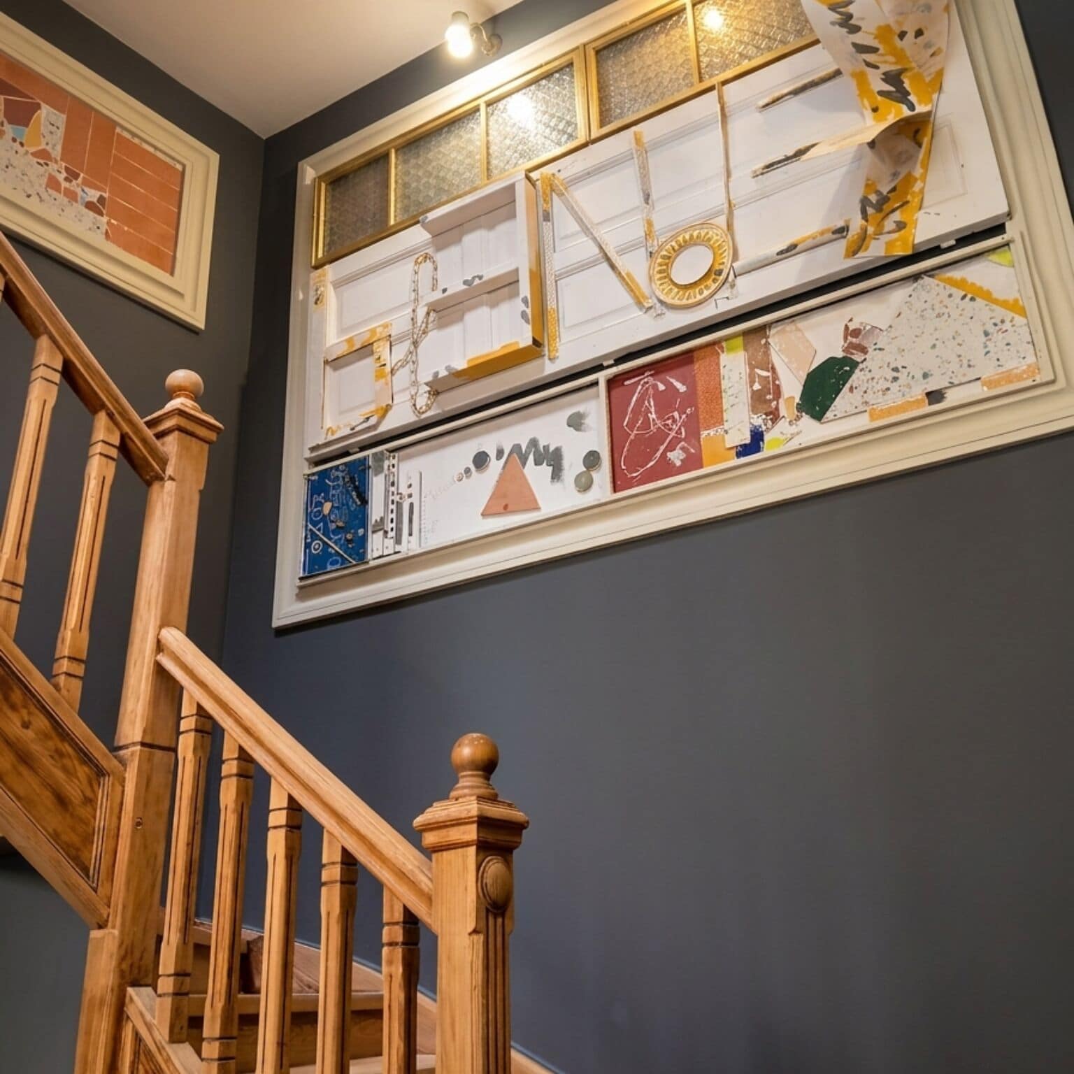 Escadaria com balaústres de madeira e corrimão, conduzindo a um quarto com uma grande janela exibindo diversas obras de arte.