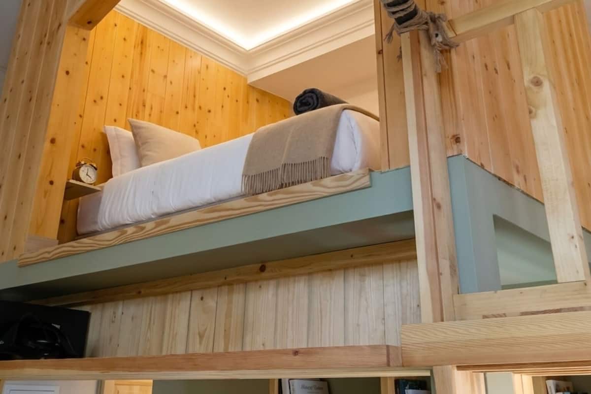 A bunk bed with a wooden headboard, a ceiling light fixture, and a small clock on the nightstand.