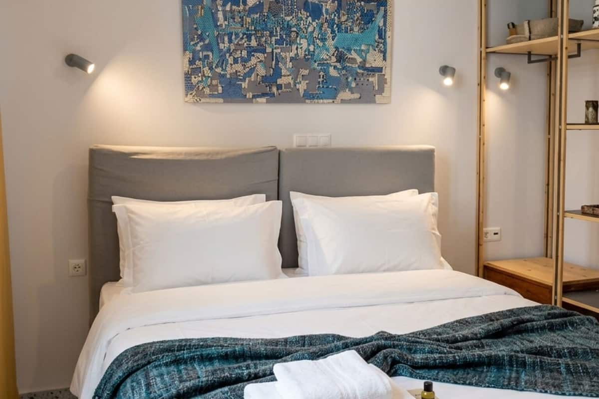 A hotel room with a bed, a headboard, a wall-mounted artwork, and a wooden wardrobe.
