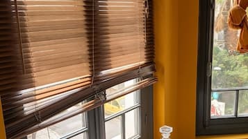 Una habitación con una mesa de madera, una tetera, una taza de café, una bandeja con libros y una ventana con persianas.