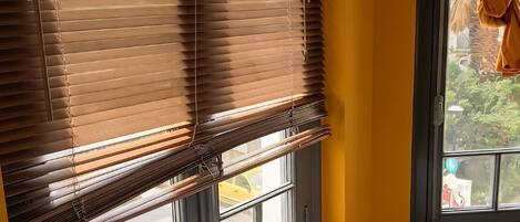 A room with a wooden table, a kettle, a cup of coffee, a tray with books, and a window with blinds.