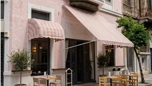 A pink building with a corner awning, outdoor seating, and a tree.
