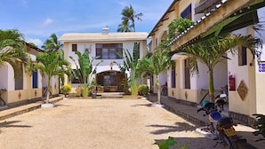 A courtyard with a central building, surrounded by palm trees and a motorcycle. - Simba Apartments Diani  (Ukunda)