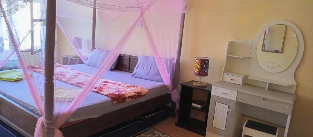A bedroom with a four-poster bed, a bedside table with a lamp, a mirror, and a dresser.