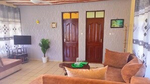 A living room with a sofa, a television, a potted plant, and a door. - Simba Apartments Diani  (Ukunda)