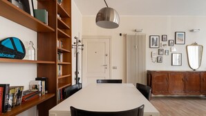 Ein Essbereich mit einem weißen Tisch, schwarzen Stühlen, einem Holzregal und einer Heizung.