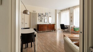 Ein modernes Wohnzimmer mit Essbereich, einer Couch, einem Holzschrank und einem großen Fenster mit Vorhängen.
