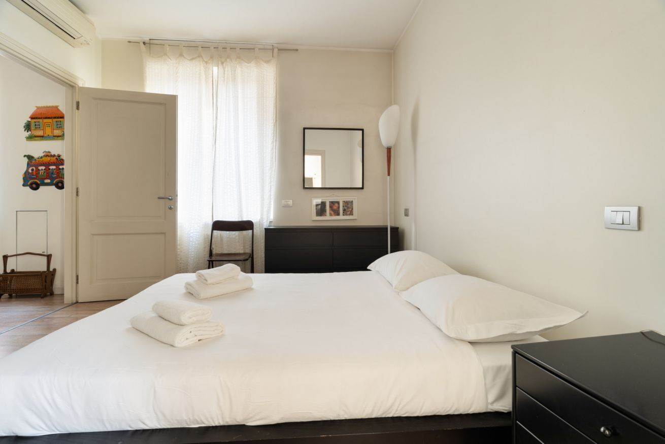 A bedroom with a bed, a bedside table, a dresser, a mirror, and a door.