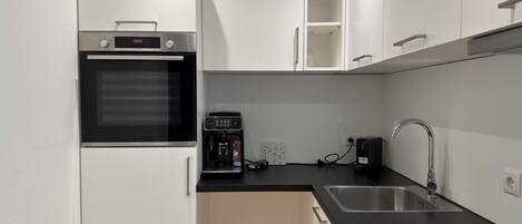 A compact kitchen with a built-in oven, a coffee machine, a sink, and white cabinetry.