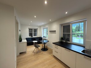 A modern kitchen with a dining area, a sofa, and large windows.
