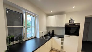 Una cocina moderna con encimera negra, armarios blancos, horno integrado y ventana con persianas.