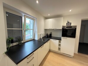 A modern kitchen with a black countertop, white cabinets, a built-in oven, and a window with blinds.