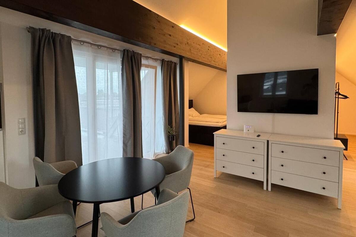 Une chambre moderne équipée d’un lit, d’une télévision, d’une table à manger avec des chaises et d’un petit coin cuisine.